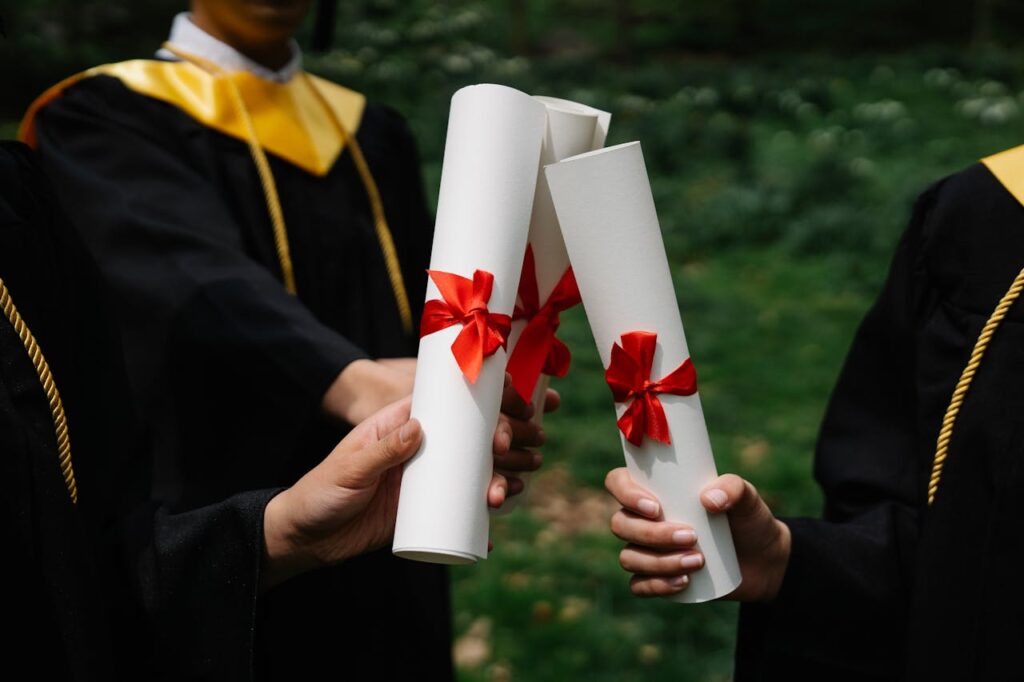 Group of graduates holding diplomas with red ribbons during a ceremony outdoors.